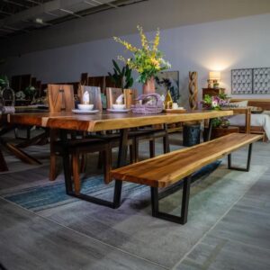 Solid Wood Furniture. Best wood furniture in Canada. Gowera. Wooden dining table with matching bench and chairs, decorated with plates, bowls, and a flower arrangement, set in a warmly lit showroom with other wooden furniture pieces in the background.